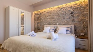 Ein Schlafzimmer mit Steinwand, einem Bett mit gestreiften Kissen und einem weißen Kleiderschrank.