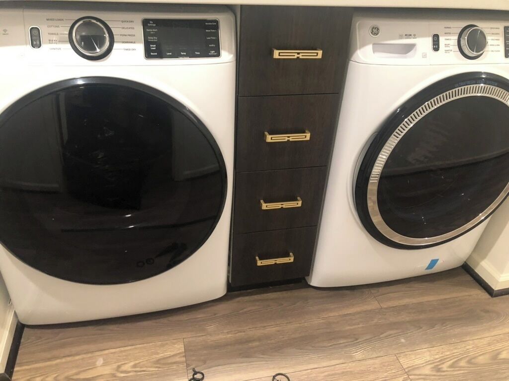 A front view of a washing machine and dryer unit with control panels and a wooden floor.