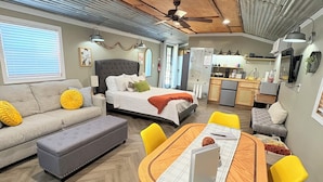 Un espacio habitable compacto con comedor, kitchenette y un dormitorio con cama grande y ventilador de techo.