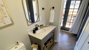 Un baño con inodoro blanco, lavamanos con grifo dorado, espejo y una toalla colgada en la pared.