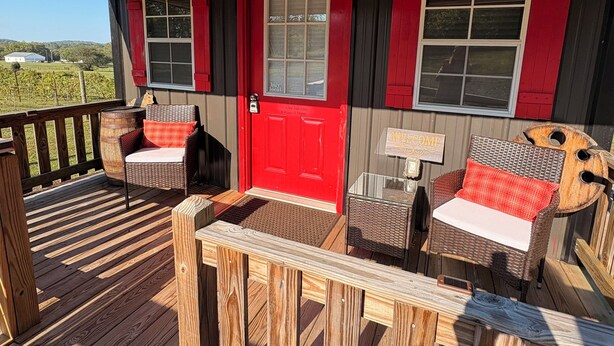 Un porche cubierto con una puerta roja, dos ventanas y muebles de mimbre.