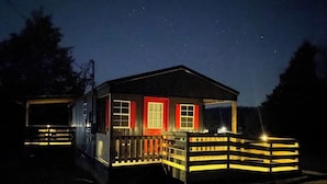 Una pequeña caba ña de dos pisos con puerta roja y ventanas, rodeada por una valla de madera.