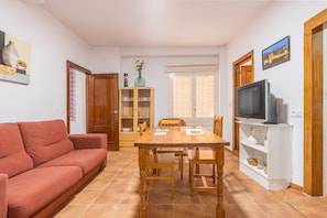 Una sala de estar con sofá, mesa de comedor, sillas, televisor y aparador.