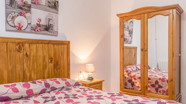 Une chambre à coucher avec une tête de lit en bois, un lit avec une literie à motifs floraux, une table de chevet avec une lampe et une armoire avec un miroir.