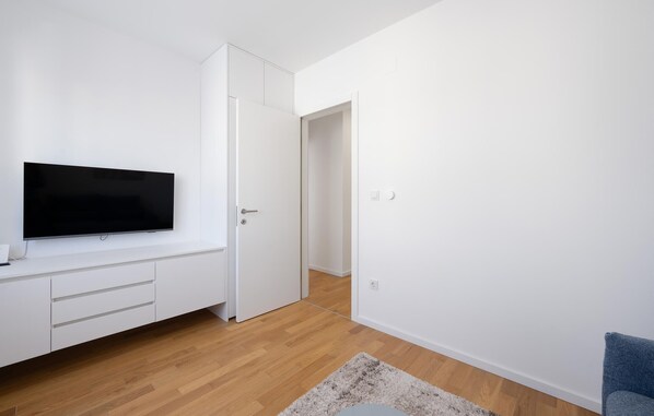A modern, minimalistic room with a flat-screen TV mounted on a white wall, a wooden floor, and a blue chair.