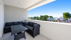 Ein Balkon mit einer Couch und einem Tisch, mit Blick auf eine Wohngegend mit Häusern und Bäumen.