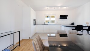 Eine moderne Küche mit weißen Schränken, einer schwarzen Arbeitsplatte und einem Essbereich mit einem Glastisch und Stühlen.