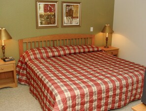 A neatly made bed with a checkered bedspread, two bedside lamps, and two framed pictures on the wall.
