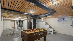 A room with a foosball table, a dining area with chairs, a staircase, and a small window. - Heritage House in Pittsburgh on Mt Washington - Charming 3BR, 2.5b Sleeps 7+ (Pittsburgh)