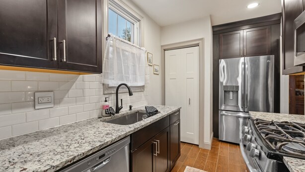 A modern kitchen with dark cabinets, a stainless steel refrigerator, a gas stove, and a window with a white curtain. - Heritage House in Pittsburgh on Mt Washington - Charming 3BR, 2.5b Sleeps 7+ (Pittsburgh)