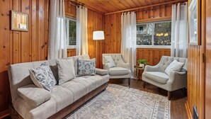 A cozy room with wooden walls and ceiling, a beige sofa with patterned cushions, two armchairs, a small table with a lamp, and a patterned rug. - Heritage House in Pittsburgh on Mt Washington - Charming 3BR, 2.5b Sleeps 7+ (Pittsburgh)