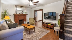 A living room with a sofa, coffee table, TV, fireplace, and staircase. - Heritage House in Pittsburgh on Mt Washington - Charming 3BR, 2.5b Sleeps 7+ (Pittsburgh)