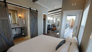 Une chambre avec un grand lit, une salle de bain avec un lavabo et un miroir, et une vue sur une terrasse et un espace extérieur.