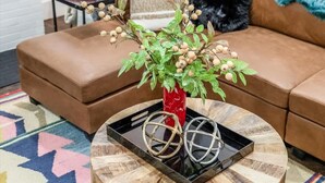 A living room with a brown sofa, a round coffee table with a plant, a lamp, and a colorful rug. - Spacious Detroit Home • Parking • Near Downtown (Detroit)