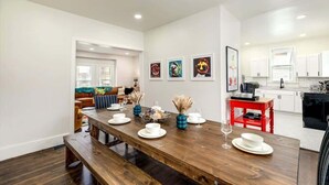 A modern kitchen with white cabinets, a wooden dining table set with white plates, and a red side table. - Spacious Detroit Home • Parking • Near Downtown (Detroit)
