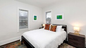 A bedroom with a bed, two bedside tables, and two windows with blinds. - Spacious Detroit Home • Parking • Near Downtown (Detroit)