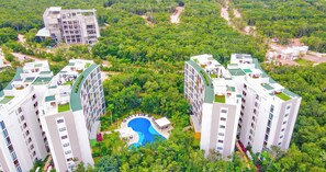 Ett högt bostadshuskomplex med flera balkonger, en central pool och frodig grönska i omgivningen.