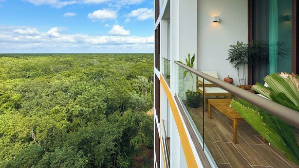 A balcony with a view of dense green forest, a wooden table, and a chair. - Bosques de Ciudad Mayakoba (Playa del Carmen)
