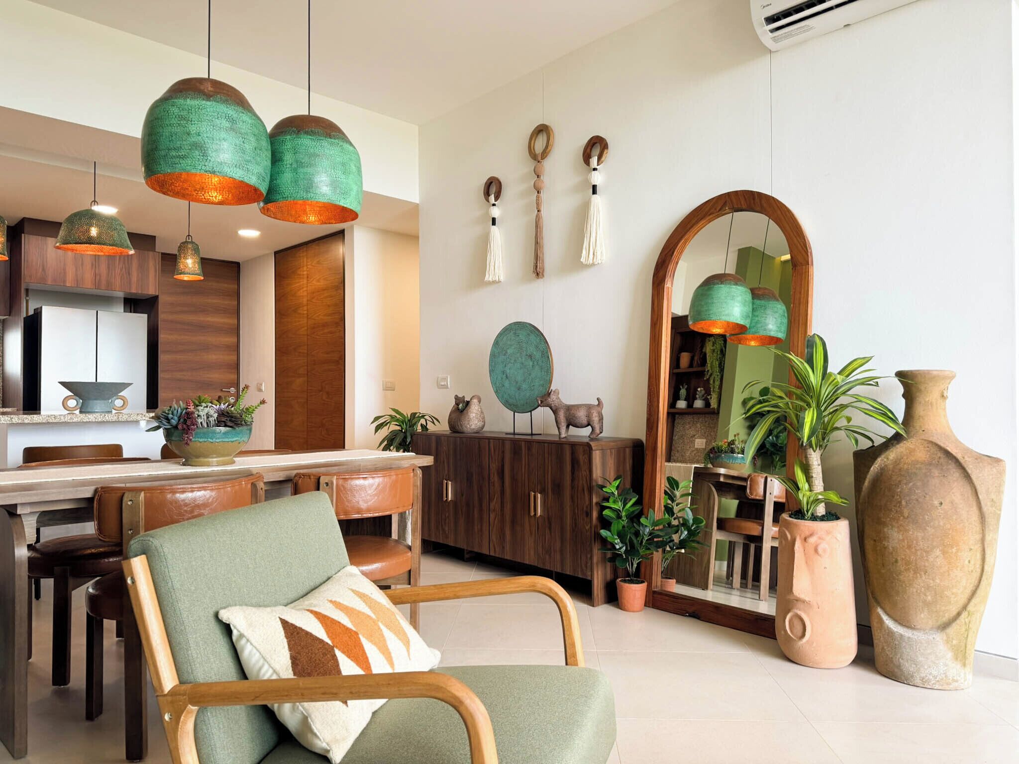 Uma cozinha moderna com armários de madeira, uma mesa de jantar e luminárias pendentes verdes.