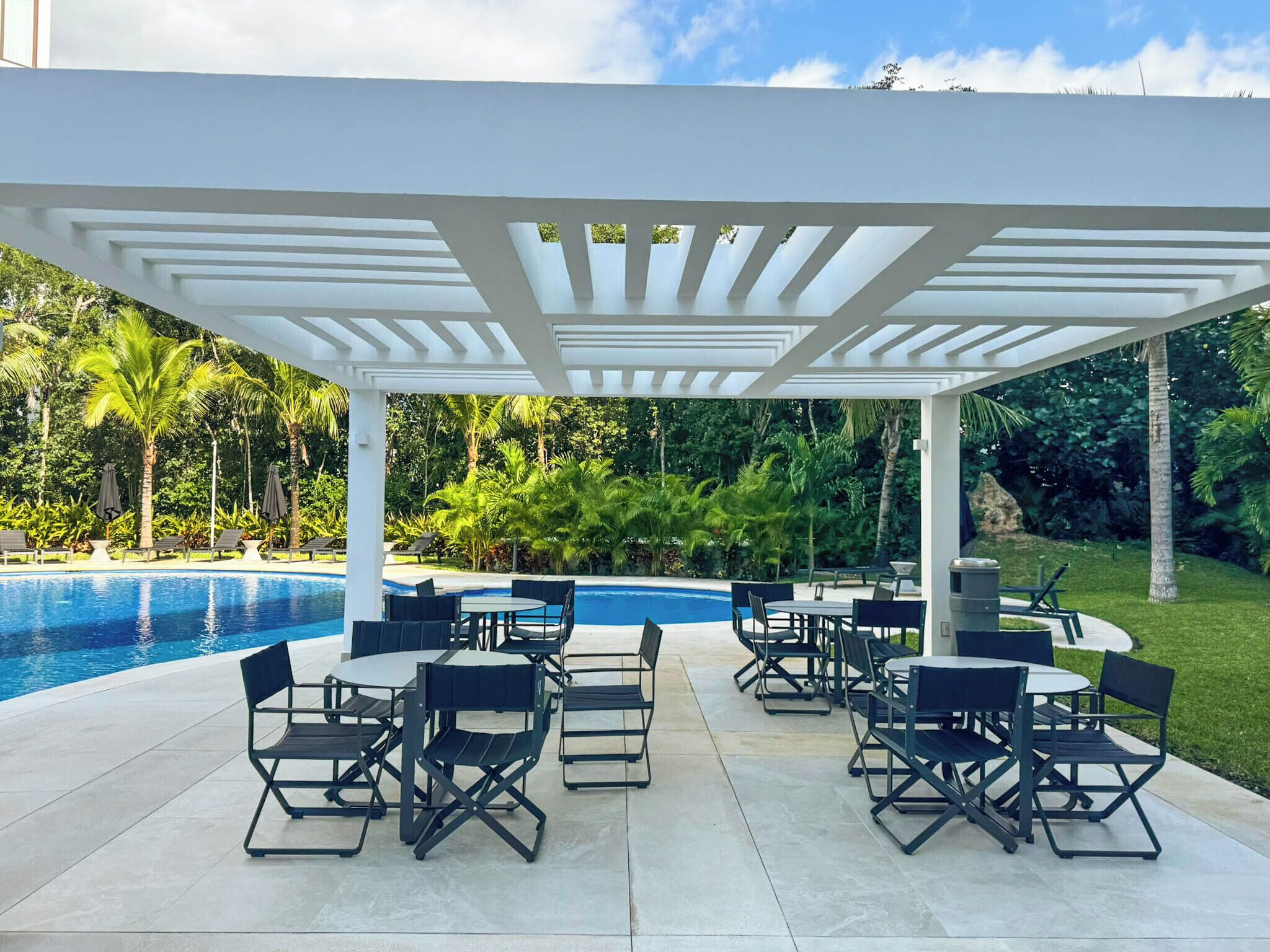 A covered outdoor area with a pool, lounge chairs, and tables.