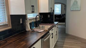 A modern kitchen with white cabinets, a dark wooden countertop, and a stainless steel sink.