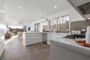 A modern kitchen with white cabinetry, a large island, and a view to the outside.