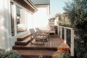 A wooden deck with outdoor furniture, a railing, and a view of the surrounding greenery.