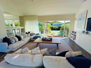 Ein modernes Wohnzimmer mit einem Ecksofa, einem Couchtisch und einem Fernseher. Es gibt einen Balkon mit Blick auf Grünflächen und ein Gebäude.