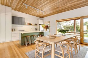 A modern kitchen with wooden flooring, a central island with stools, and a dining table with chairs. - Ivy Tyrone -Gas heated Pool, Stunning renovation (Rye)