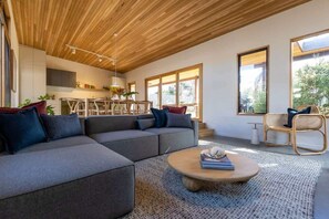 A modern living room with a sectional sofa, a coffee table, and a dining area with chairs. - Ivy Tyrone -Gas heated Pool, Stunning renovation (Rye)