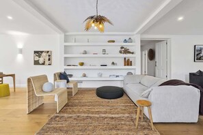 Ein modernes Wohnzimmer mit einer Couch, einem Sessel, einem runden Hocker und einer Pendelleuchte.