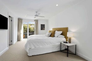Une chambre à coucher avec un lit, une table de chevet, un ventilateur de plafond et une vue sur l’extérieur.