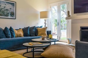 Ein Wohnzimmer mit blauem Sofa, rundem Couchtisch, Lampe, Kamin und einem an der Wand befestigten Fernseher.