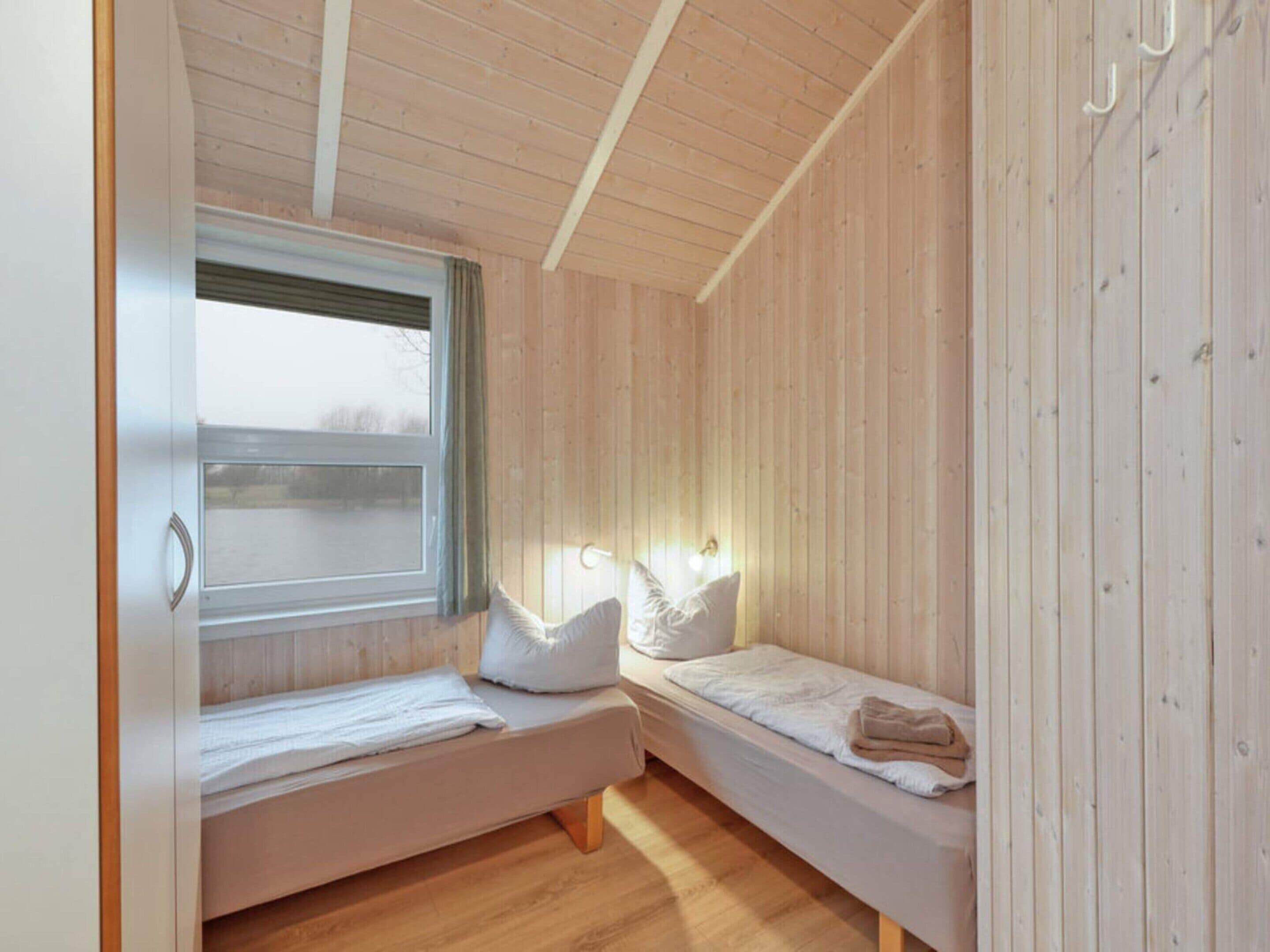 Una habitación pequeña y acogedora con dos camas individuales, paredes de madera, una ventana con cortinas y techo de madera.
