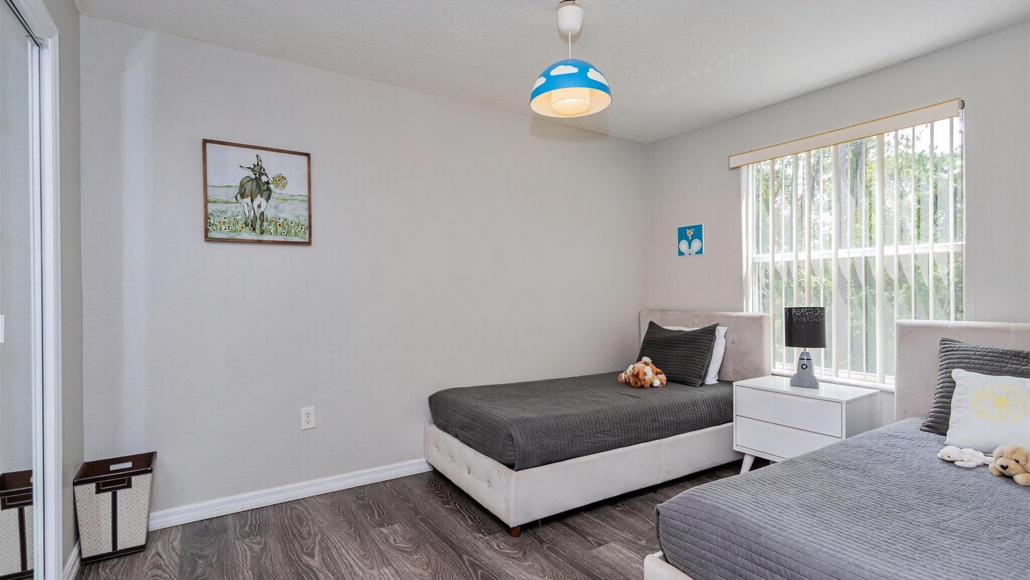 A bedroom with a bed, bedside table, lamp, and a window with blinds.