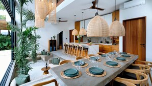 Uma área de jantar moderna com uma mesa comprida posta para seis pessoas, rodeada por cadeiras de madeira.