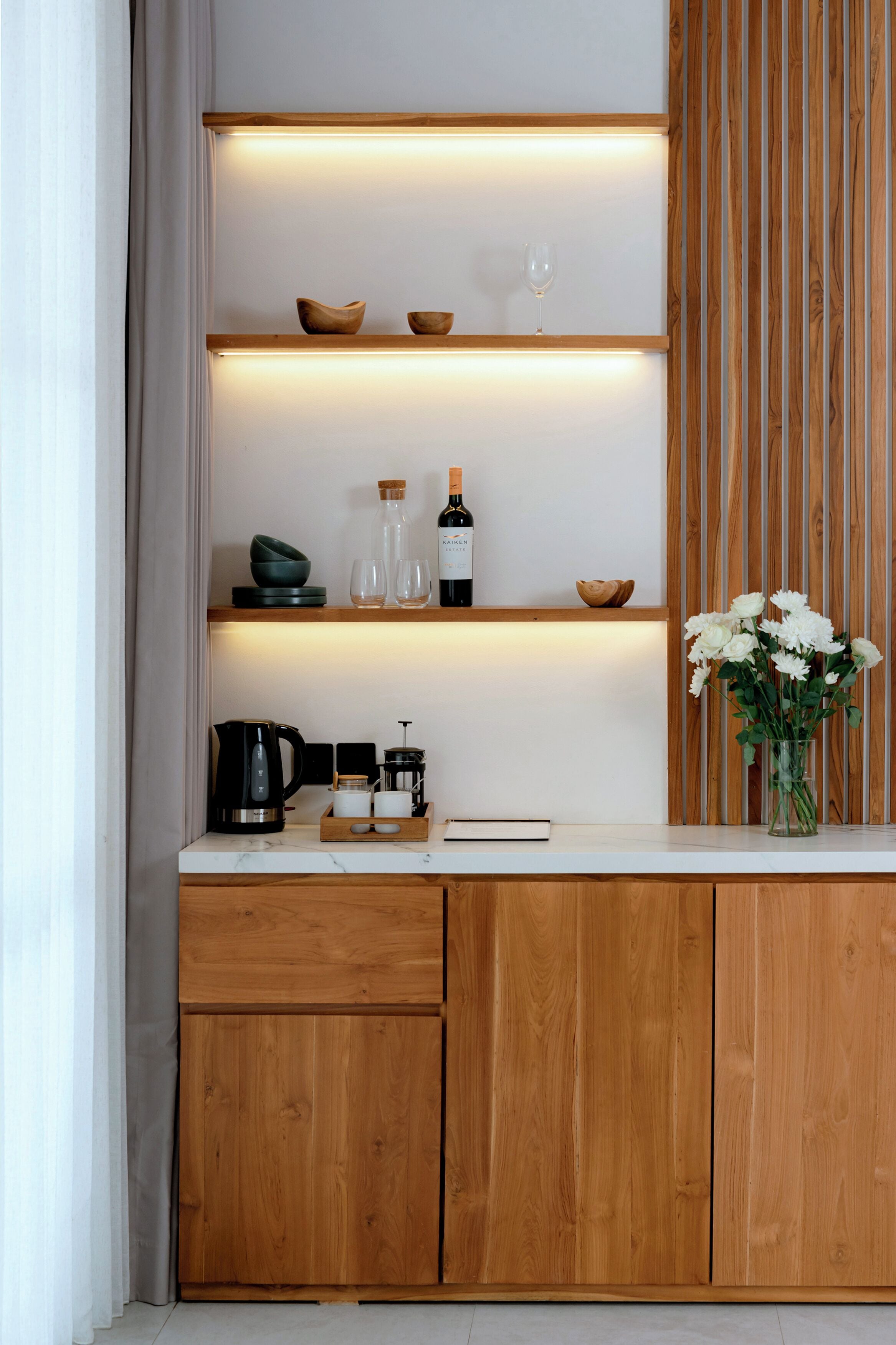 Eine moderne Küche mit Holzschränken, einer Marmorarbeitsplatte und eingebauten Regalen mit Küchenutensilien und einem Blumenstrauß.