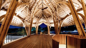 Um deck de madeira com estrutura de telhado em bambu, área de estar e vista do céu noturno.