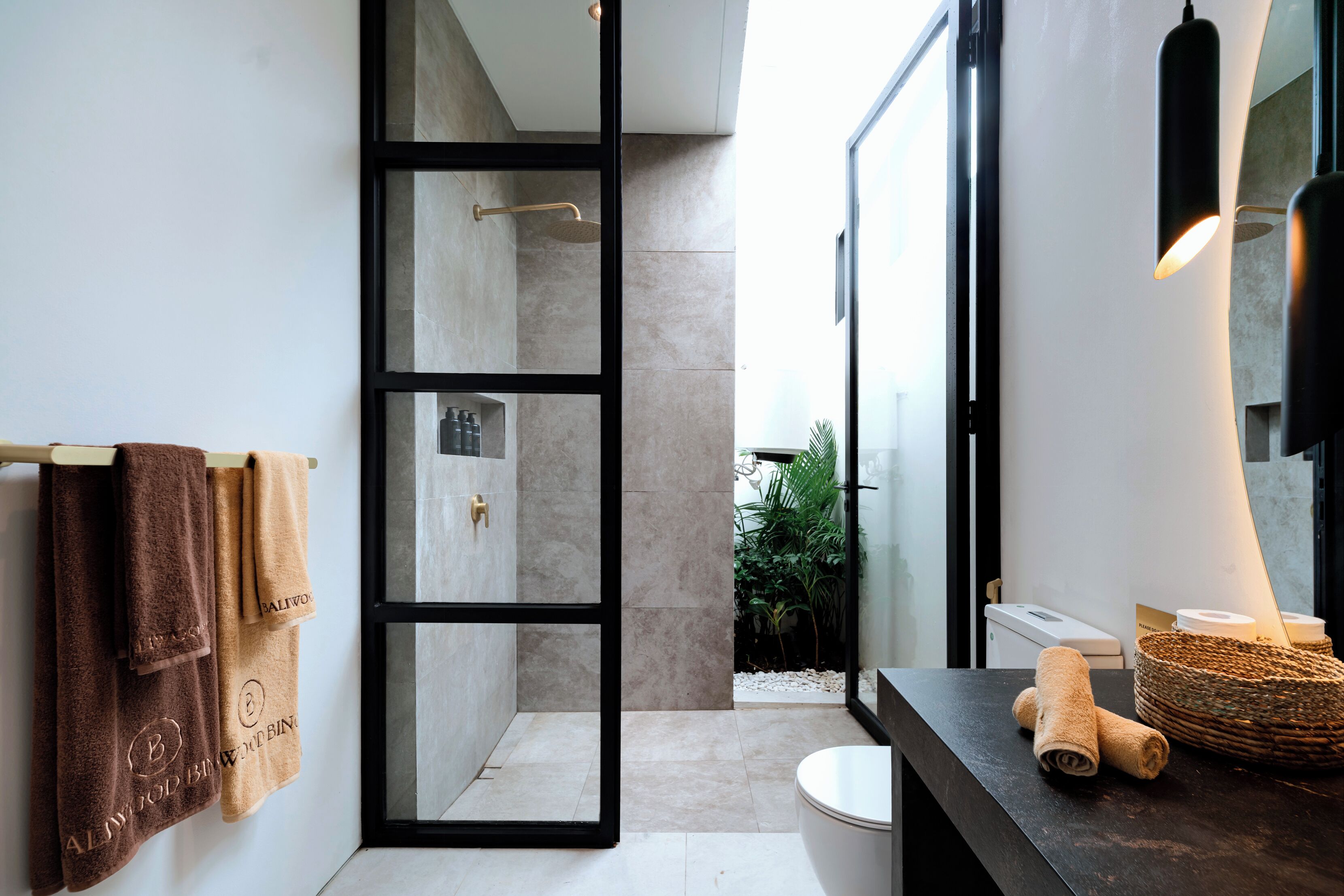 Un baño moderno con cabina de ducha de vidrio, un espejo con marco negro y un mostrador oscuro con una cesta tejida.