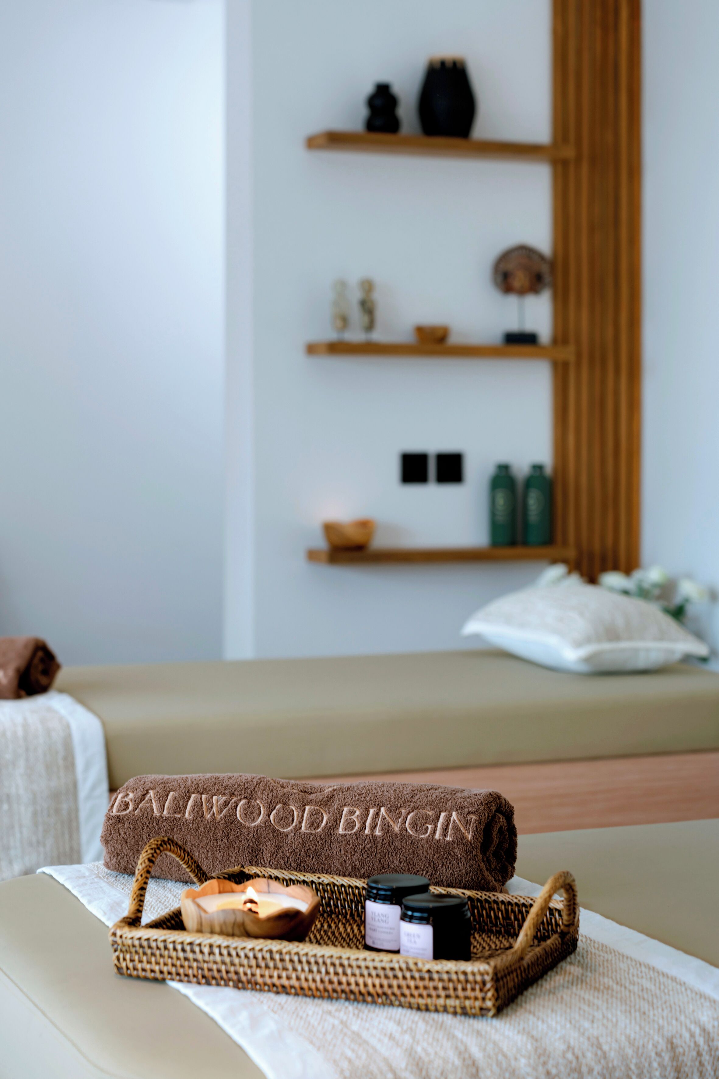 A neatly arranged spa area with a massage table, a towel labeled "Baliwood BINGIN", and a basket containing spa products.