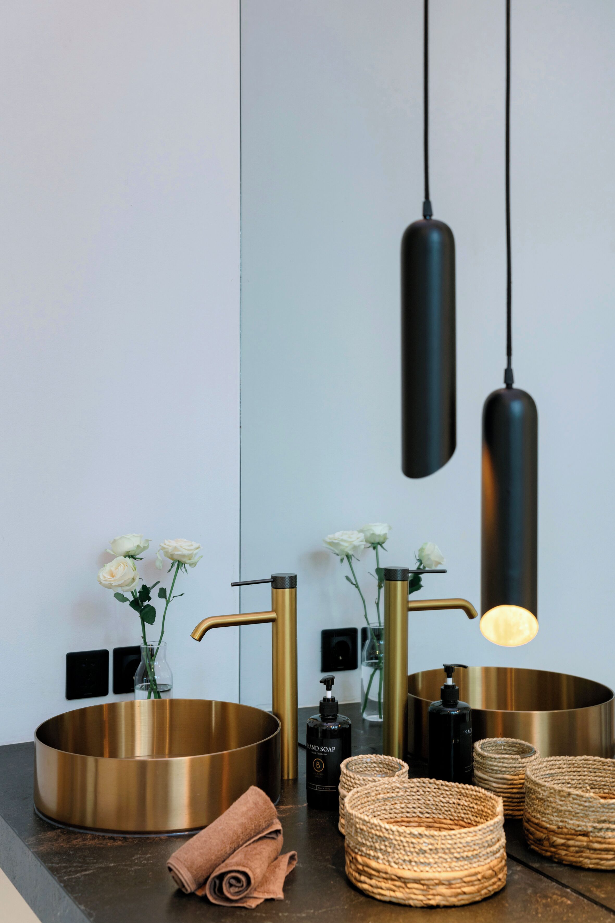 A bathroom with a round, gold-colored sink, two black pendant lights, and a mirror.