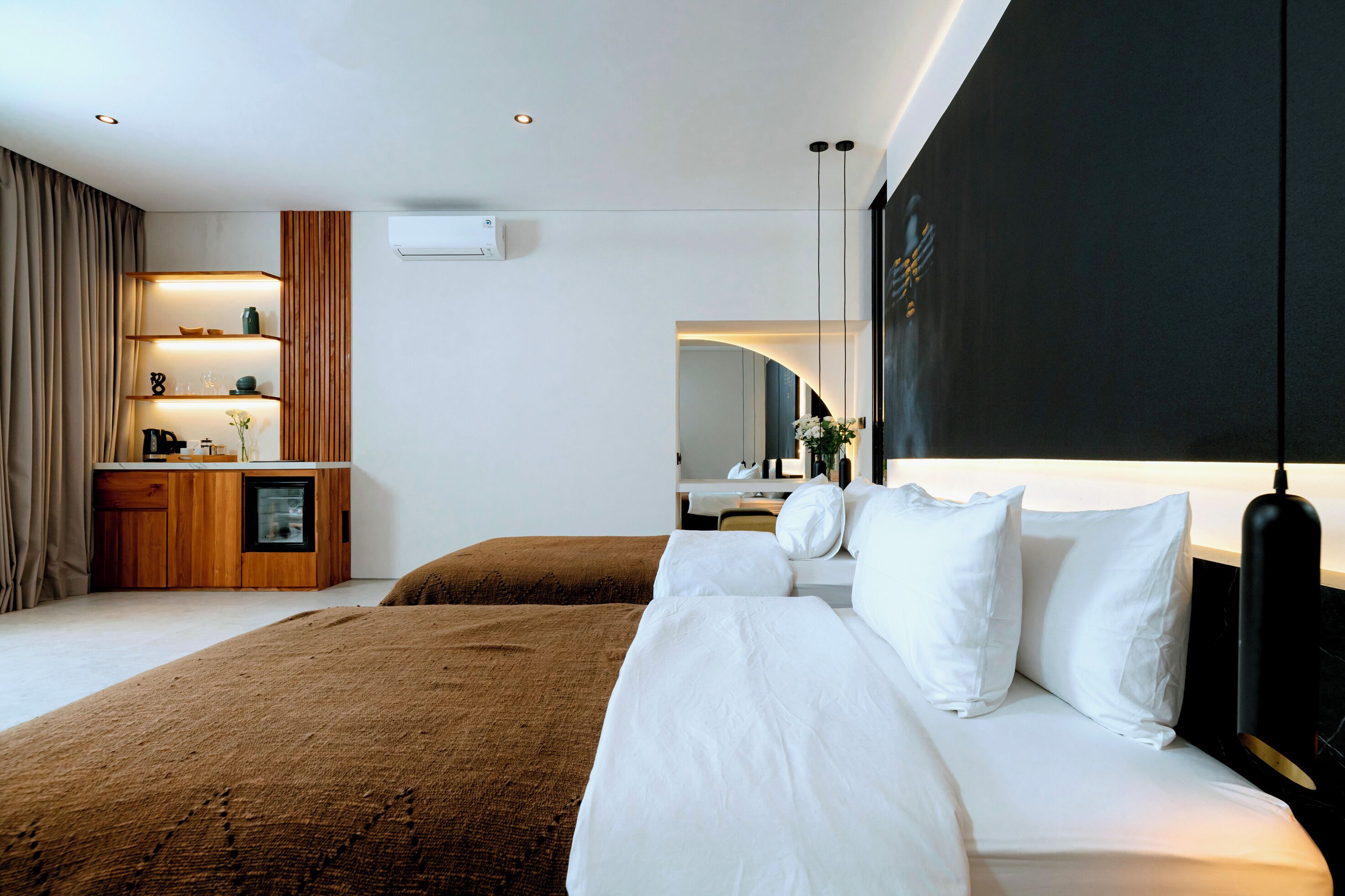 Une chambre d’hôtel moderne avec un grand lit, une table de chevet en bois, une étagère intégrée et un grand miroir.