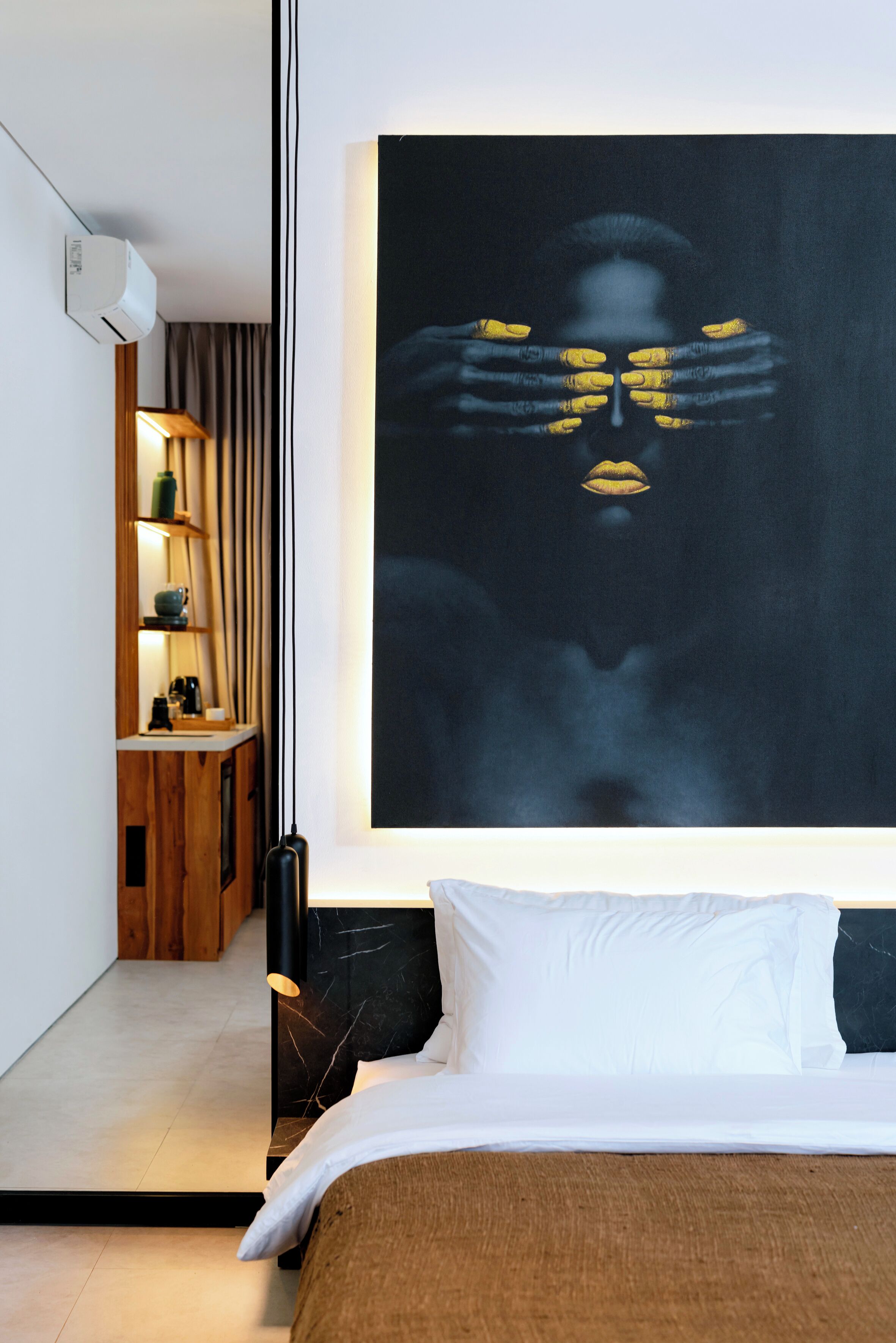 Camera d'albergo moderna con un'ampia pittura astratta, un comodino in legno con una lampada e un letto rifatto con cura.