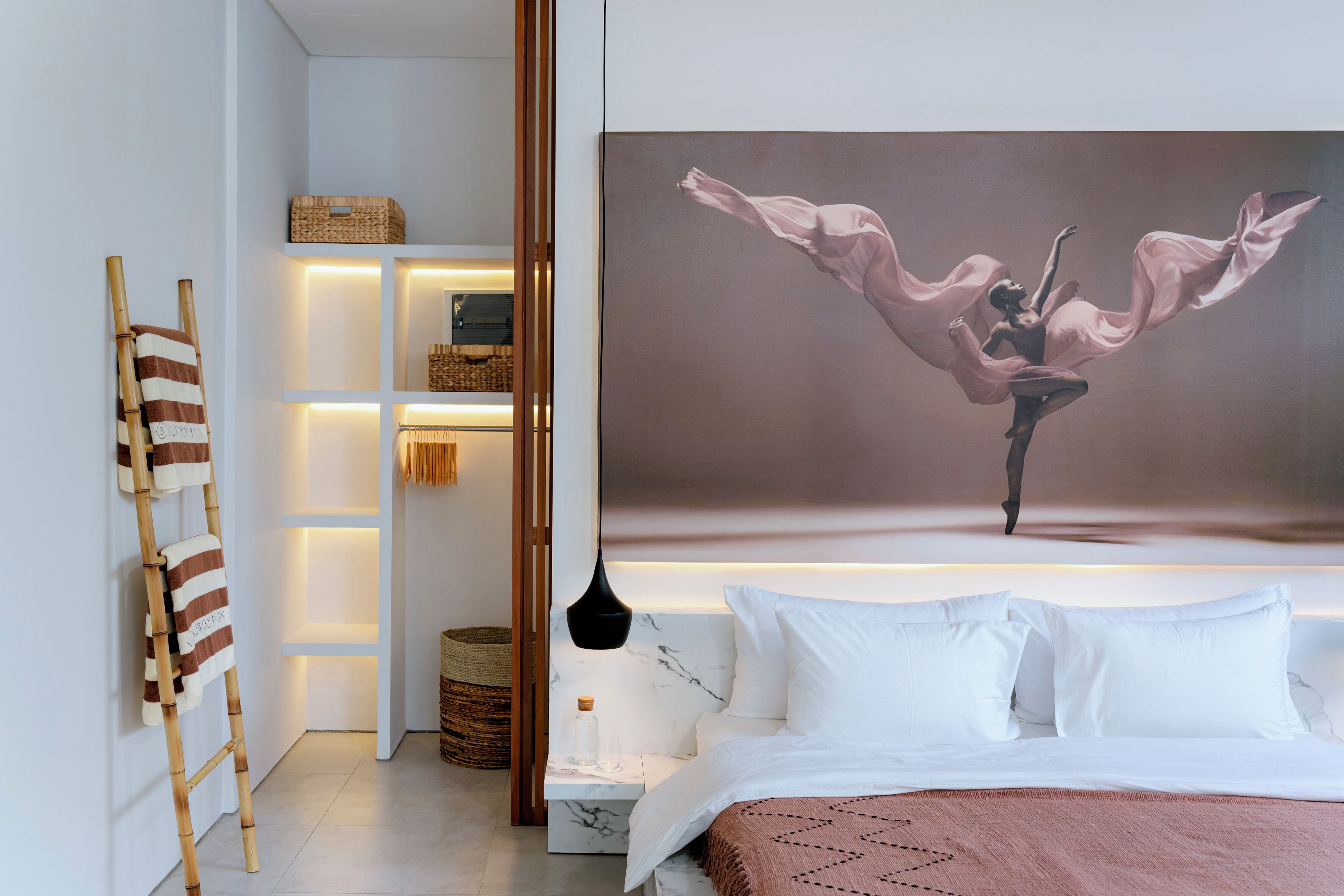 A modern bedroom with a large bed, a painting of a dancer, a wooden ladder, and a built-in shelving unit with baskets.