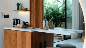 Cozinha moderna com armários de madeira, bancada branca e fogão embutido. Há prateleiras com utensílios de cozinha e uma janela com vista para áreas verdes.