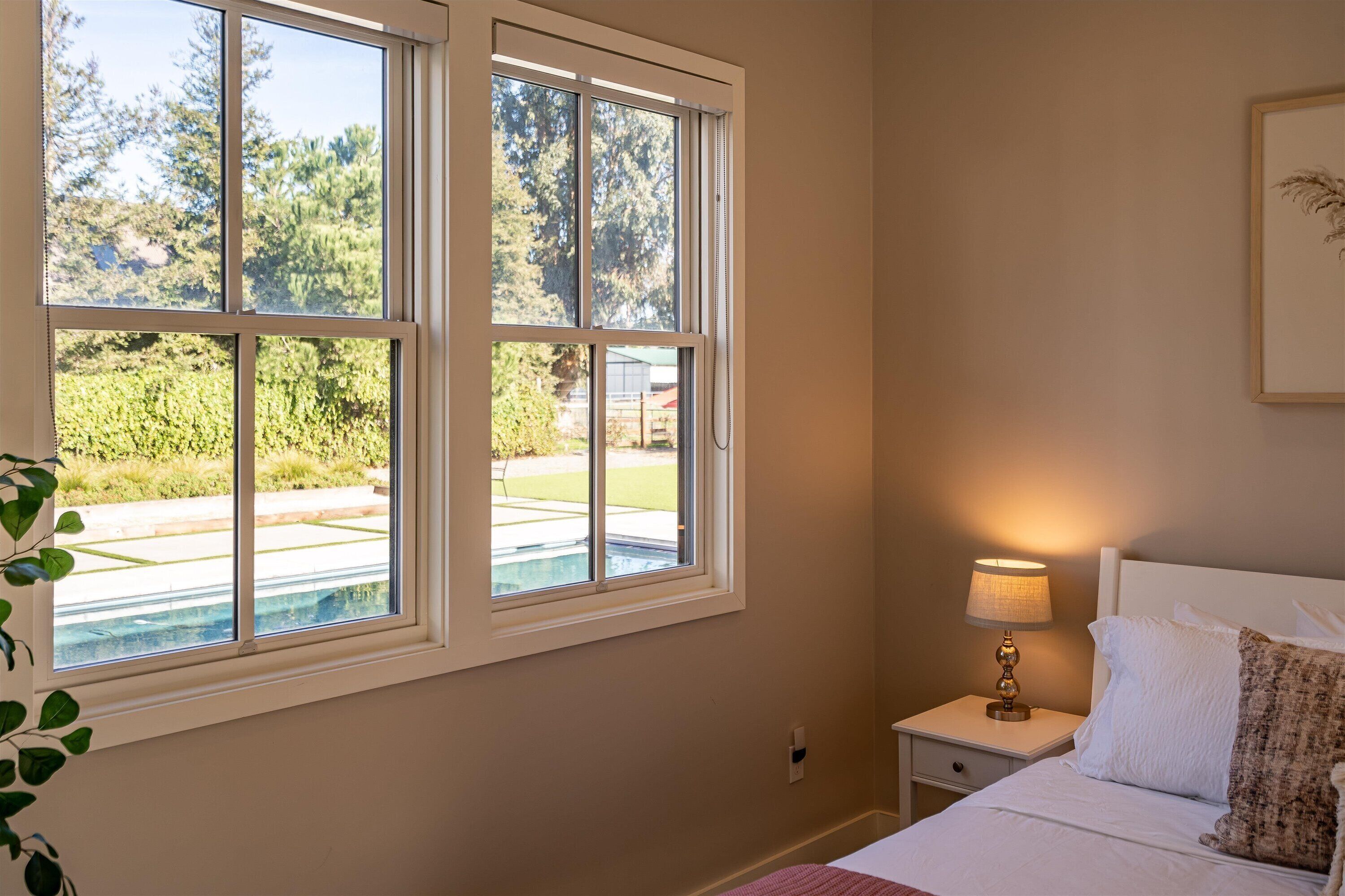 A bedroom with a large window, a bedside lamp, and a bed with pillows.