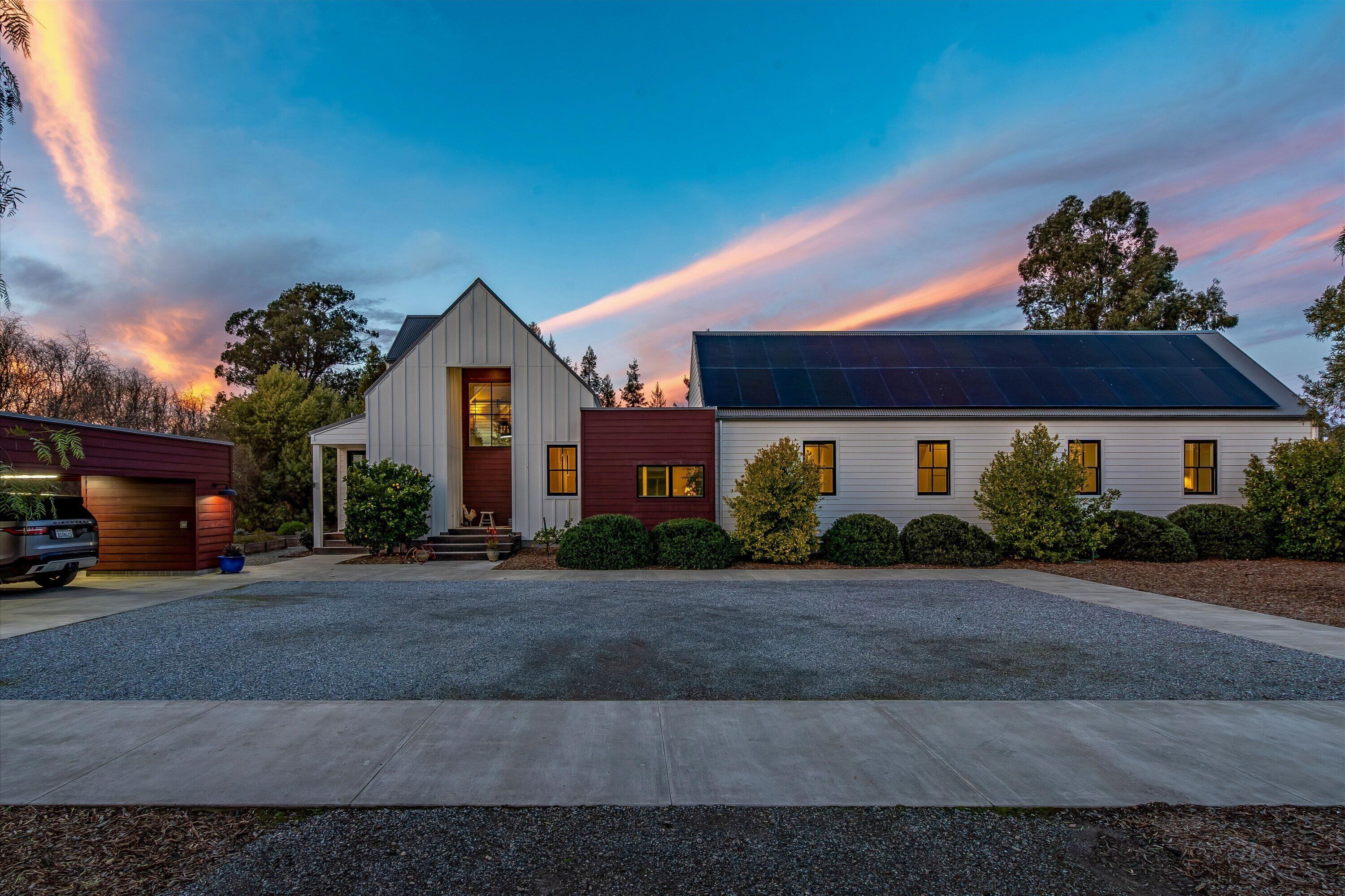 A modern two-story house with a sloped roof, solar panels, and a well-maintained driveway.