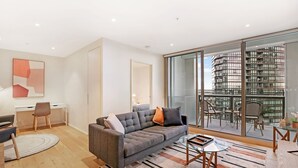 A modern living room with a grey sofa, a small coffee table, and a glass door leading to a balcony with a city view. - 888 Collins (Docklands)