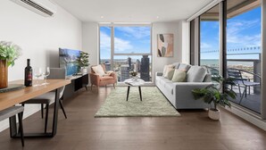 A modern living room with a dining area, large windows, and a city view. - 888 Collins (Docklands)