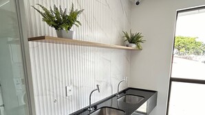 A modern bathroom with a black countertop sink, white tiled walls, and a potted plant on a shelf.